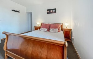 Una cama de madera con cabecera, dos mesitas de noche con lámparas y un cuadro colgado en la pared.