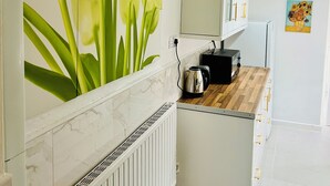 A kitchen with a marble backsplash, a radiator, a wooden countertop, a kettle, and a painting of tulips on the wall.