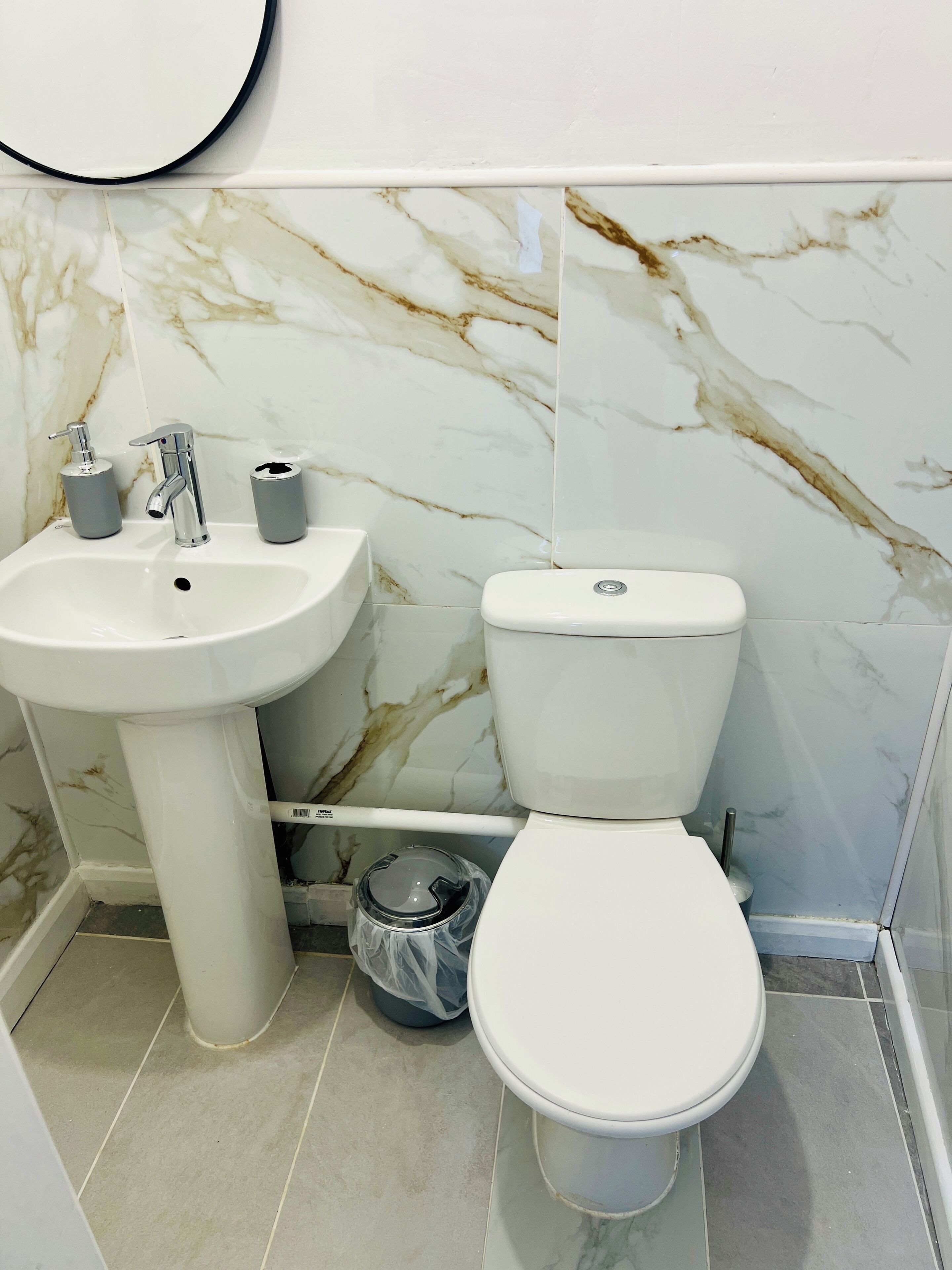 Un baño con un lavabo blanco, inodoro y pared con diseño de mármol.