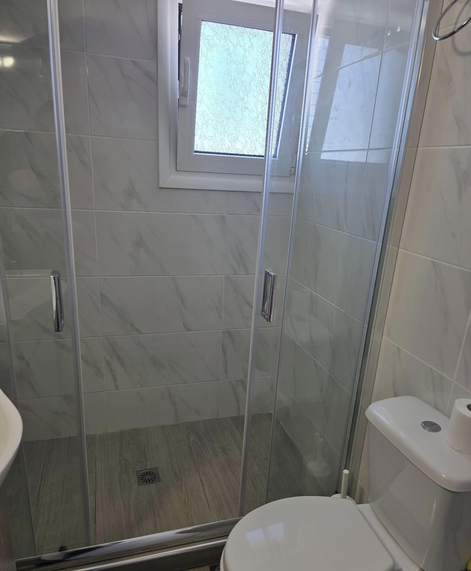 A bathroom with a glass-enclosed shower, a toilet, and a small window above the shower.