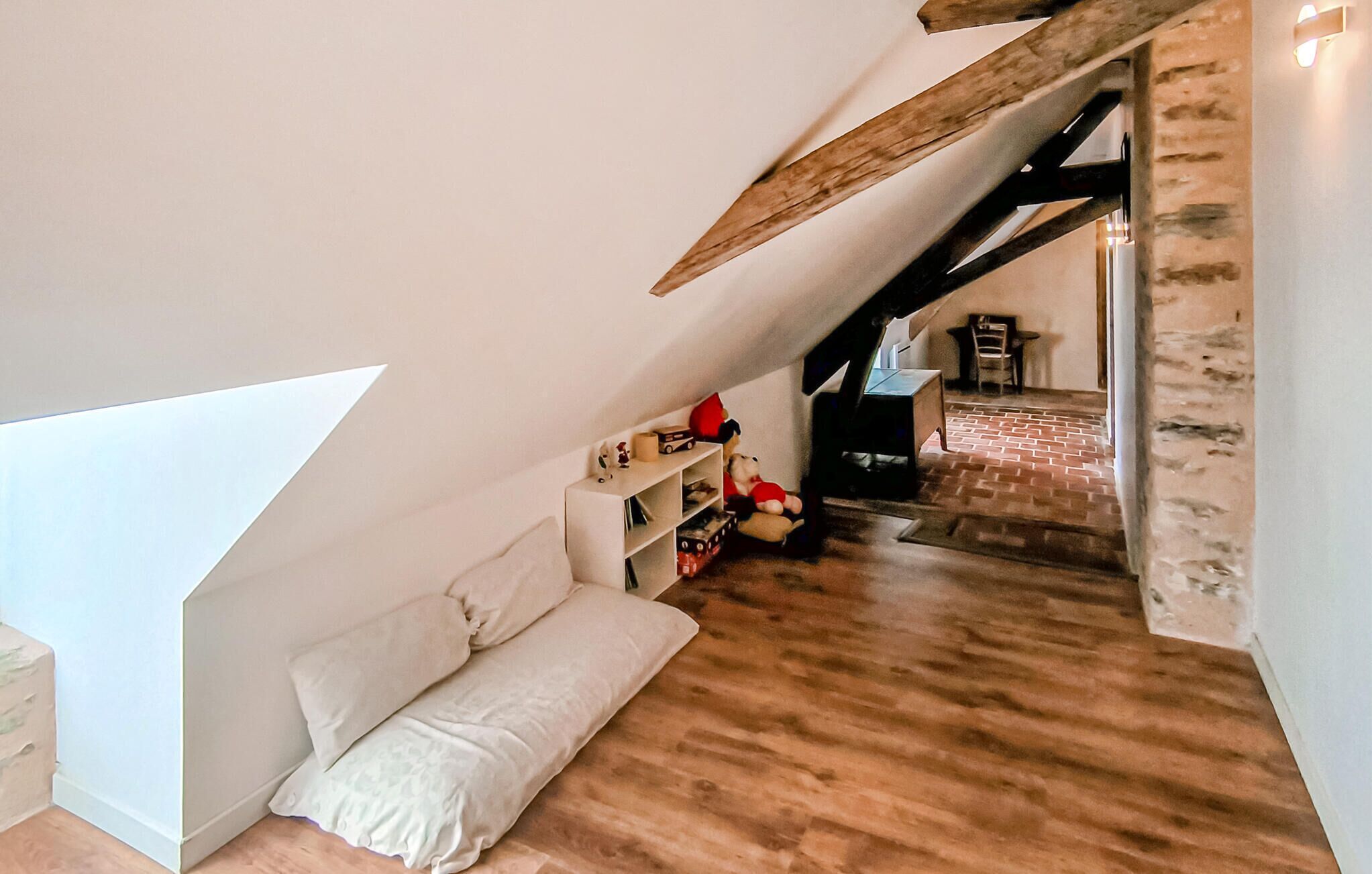 A cozy attic bedroom with a sloped ceiling, wooden flooring, and a built-in shelving unit with toys.