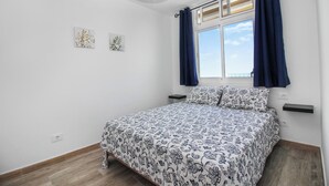 A bedroom with a bed, a window with curtains, a wall-mounted shelf, and a ceiling light fixture. - Amadores Top Views apartment (Puerto Rico de Gran Canaria)