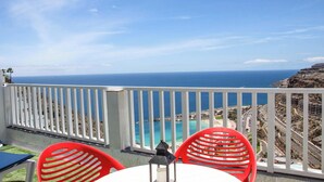 A balcony with a white railing, red chairs, and a table. - Amadores Top Views apartment (Puerto Rico de Gran Canaria)