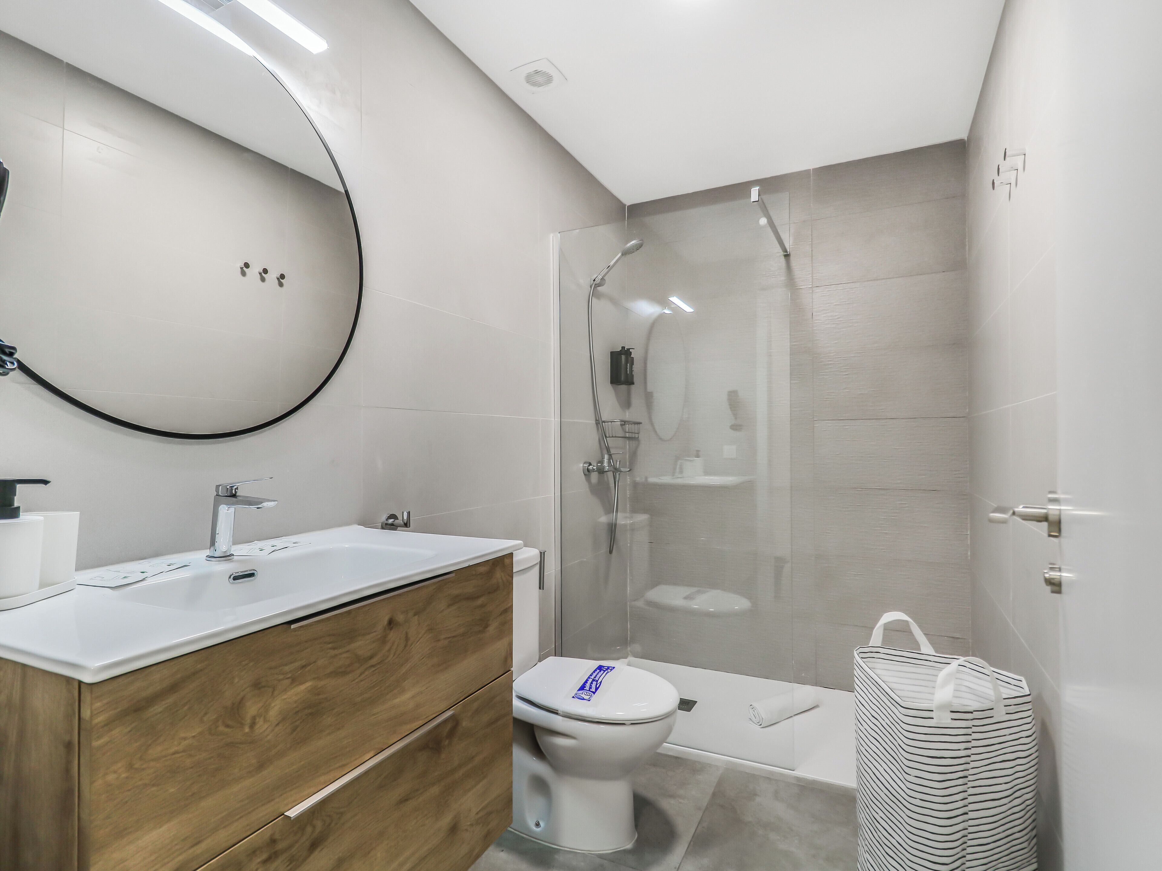 A modern bathroom with a wooden vanity, a toilet, a shower enclosure, and a white sink.