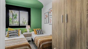 Un dormitorio con dos camas, una mesita de noche, un armario y una ventana con vistas a árboles.