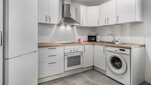 Una cocina compacta con armarios blancos, una campana extractora de acero inoxidable, un microondas, un fregadero, una lavadora y una encimera de madera.