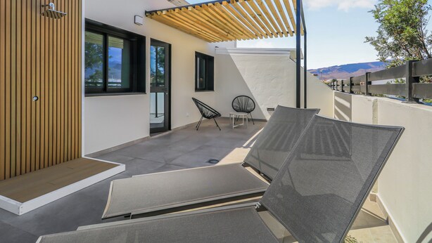 Una terraza en la azotea con una pérgola, dos sillones de descanso y un pequeño rincón de estar con dos sillas.