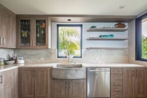 Uma cozinha moderna com armários de madeira, uma máquina de lavar louça em aço inoxidável e uma janela com vista para o verde.