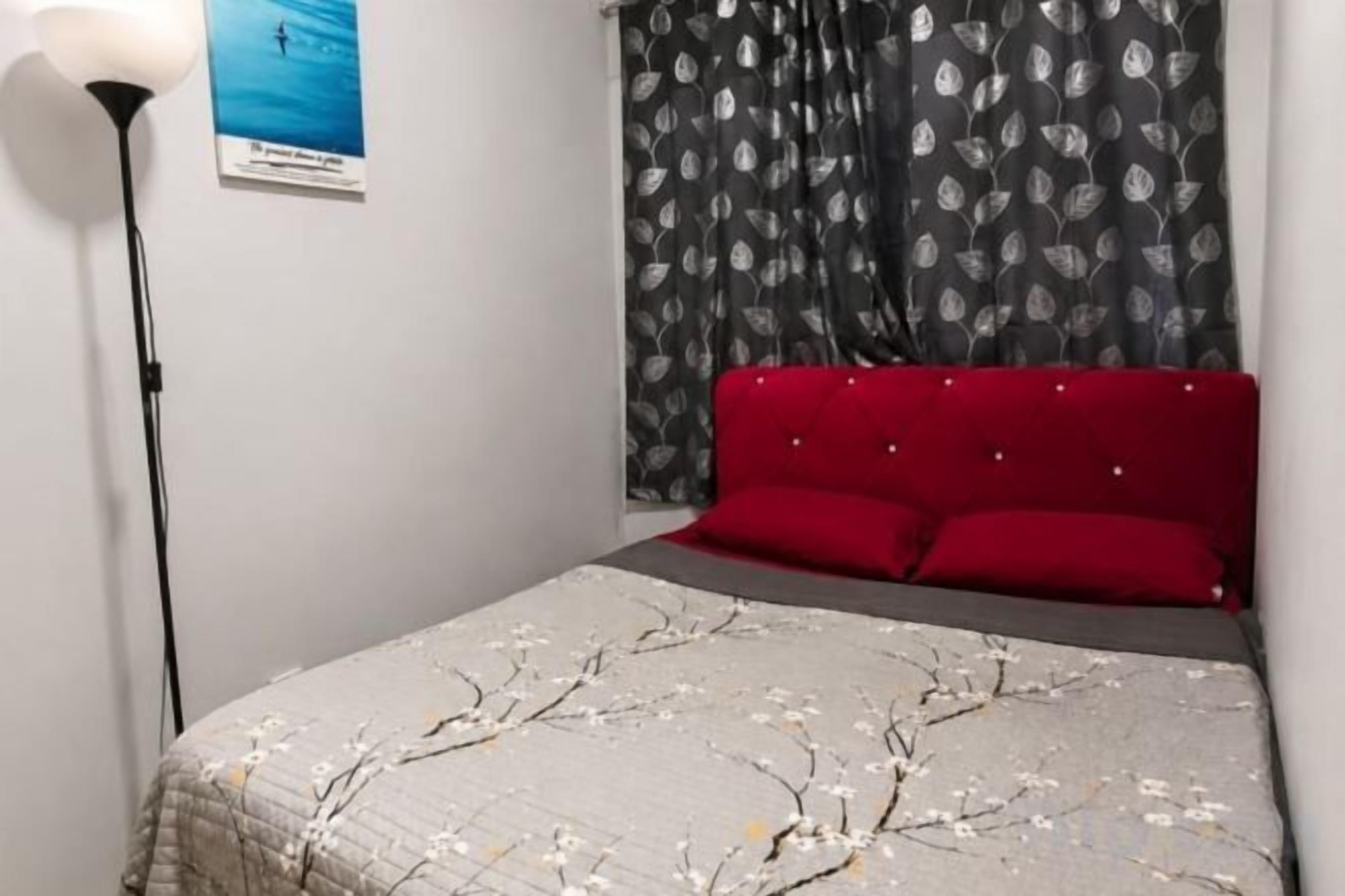 Une chambre à coucher avec un lit, une tête de lit rouge, une lampe sur pied et une affiche accrochée au mur.