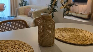 Una habitación con una mesa blanca, un jarrón tejido y individuales tejidos.