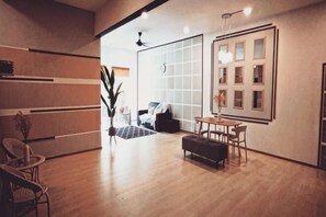 A modern interior with a wooden floor, a dining area with chairs, a table, and a large window with blinds. - Barakah Sufi Home Stay Apartment Cameron (Tanah Rata)