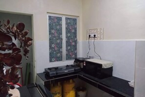 Eine kompakte Küche mit Mikrowelle, kleinem Kühlschrank und Spüle. Ein Fenster mit Dekorglas ist vorhanden, und links ist eine Pflanze zu sehen.