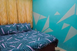 Ein Bett mit gemusterten Betttextilien, ein Vorhang und eine Wand mit geometrischen Mustern.