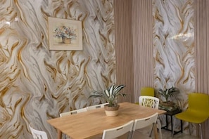 A dining area with a marble-patterned wall, a wooden table, white chairs, and potted plants. - Barakah Sufi Home Stay Apartment Cameron (Tanah Rata)