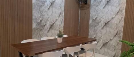 A dining area with a marble wall, a wooden table, white chairs, and a small plant.