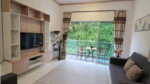 Una sala de estar con televisor, sofá, mesa de centro y balcón con vistas a zonas verdes.