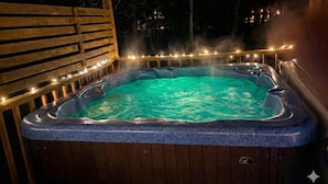 A hot tub with a wooden deck and string lights, surrounded by trees. - Ishki Creek Cabin ~Your peaceful cabin getaway (Broken Bow)