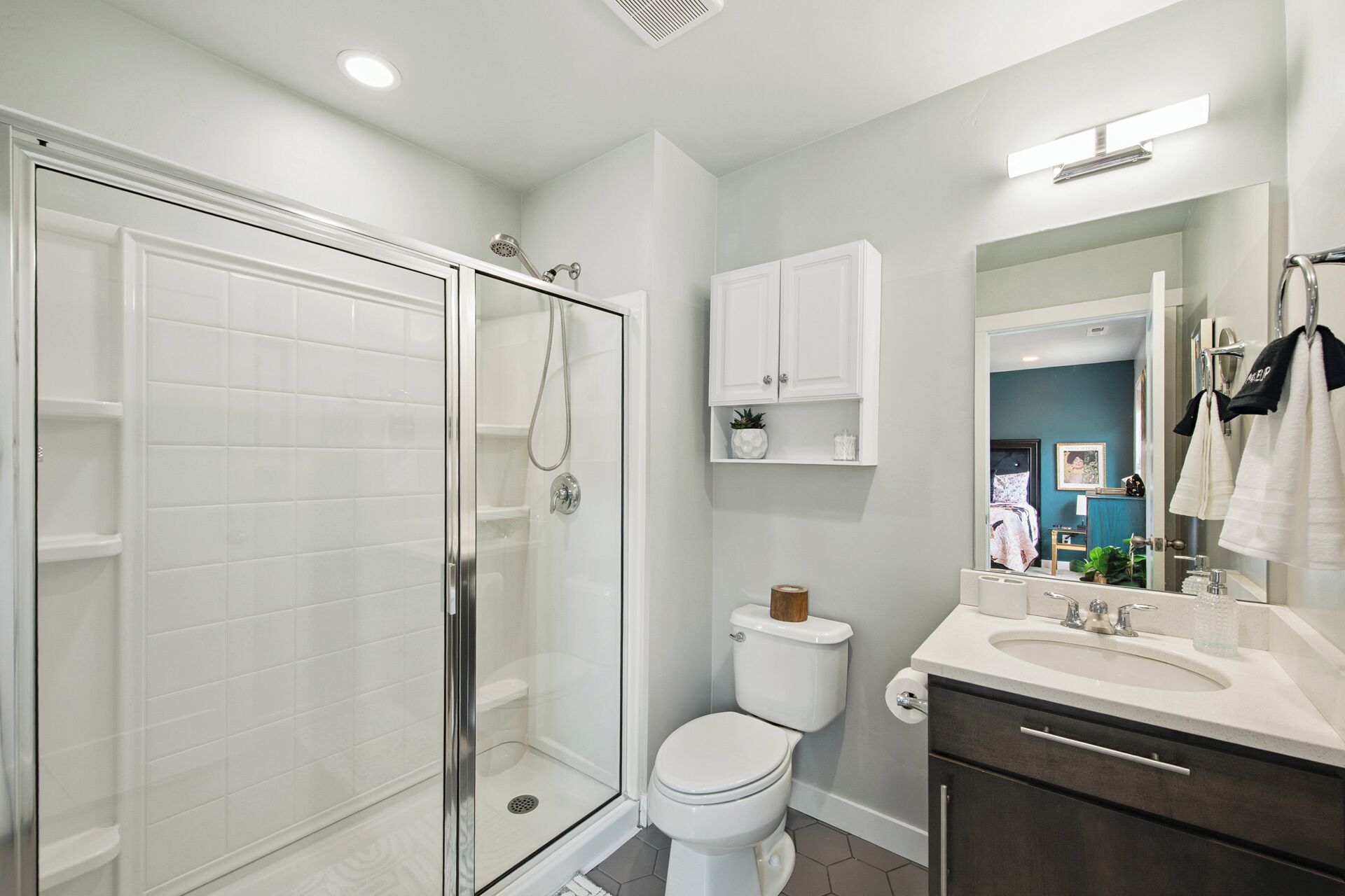 A modern bathroom with a glass-enclosed shower, a white toilet, and a vanity with a mirror and sink.