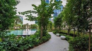 Un vialetto curato con una piscina, circondato da vegetazione lussureggiante e palazzi imponenti sullo sfondo.