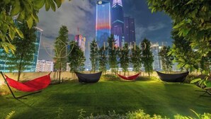 Paesaggio urbano notturno con grattacieli illuminati, una zona verde con amache e alberi.