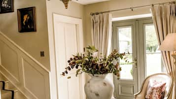 Een kamer met een trap, een kroonluchter, een vaas met bloemen, een ronde tafel en een stoel met een kussen.