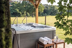 A hot tub with a wooden table and towels beside it, set on a wooden deck with a view of a grassy field and trees. - Luxury Country Estate & Farm Group Stay – Sleeps 16-18 in Ireland’s Ancient East (Lobinstown)
