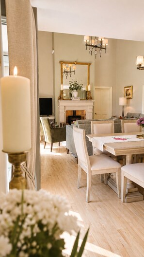 Una sala de estar bien iluminada con chimenea, un comedor con mesa y sillas, y un espejo grande sobre la chimenea.