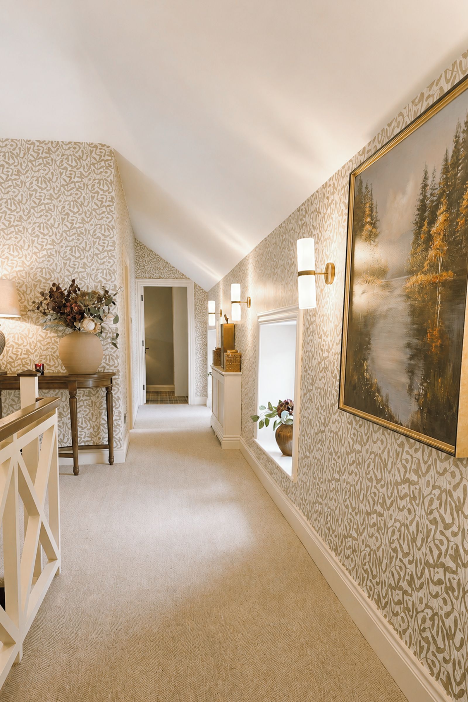 A hallway with patterned wallpaper, a painting of a forest, and a staircase leading to another room.
