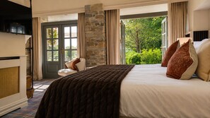 A bedroom with a large bed, a stone wall, a door leading outside, and a view of greenery.