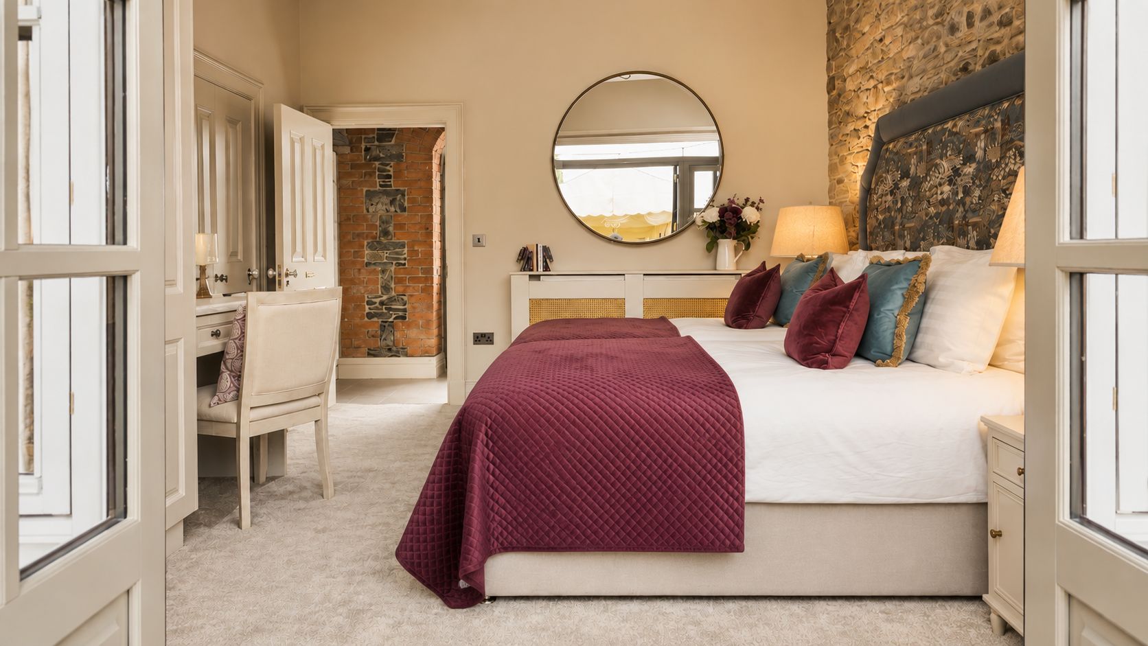 A bedroom with a bed, a dresser, a mirror, and a stone wall.