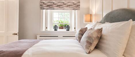 A bedroom with a bed, a window with curtains, a lamp, and a radiator.