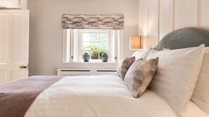 Um quarto com cama, janela com cortinas, luminária e radiador.