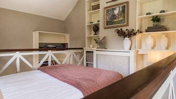Ein Schlafzimmer mit einem Bett, einem weißen Kopfstück, einem Holztisch, einer weißen Regaleinheit und einem Bild an der Wand.