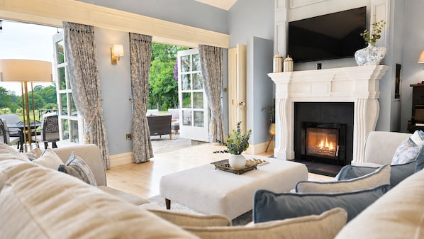 A living room with a fireplace, a sofa set, and a dining area visible through a glass door.