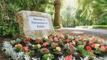 Ein Willkommensschild am Eingang des Parsonstown Estate, umgeben von einem Garten mit verschiedenen Pflanzen und Blumen.