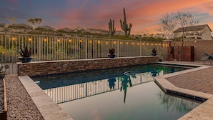 A swimming pool with a stone wall and metal railing, surrounded by desert vegetation and a sunset sky. - 119th Sun City (Sun City)