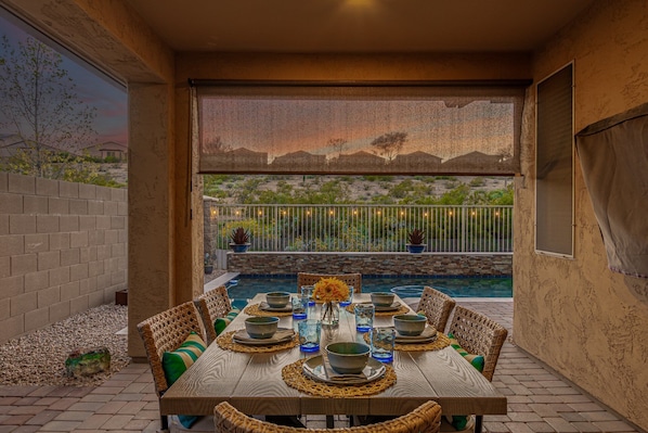 Un espace extérieur aménagé pour les repas, avec une piscine, des meubles en osier et une vue sur un paysage désertique.