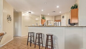 A kitchen with a central island, three bar stools, and wooden cabinets. - Blackfoot Two San Tan Valley (San Tan Valley)