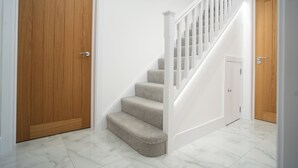 Una escalera con peldaños alfombrados y barandillas blancas, que conduce a una puerta con detalles de madera.