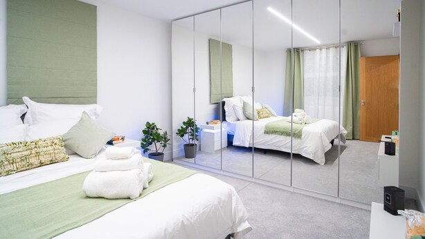 Una habitación de hotel moderna con un espejo grande, dos camas, una mesita de noche y una planta en maceta.