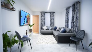 Una sala moderna con un sofá gris, dos sillones, un televisor de pantalla plana y una planta en maceta.
