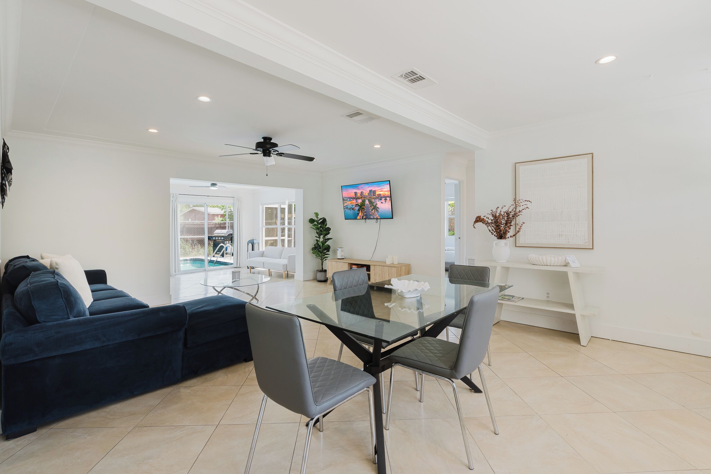 Un salon moderne avec une table à manger au plateau en verre, un canapé bleu foncé et un ventilateur de plafond.