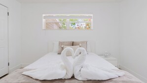 A bedroom with a bed, two nightstands, a window, and a pair of swans made of towels. - FLORIDA PARADISE / 5 MIN TO DOWNTOWN / 3BDR/6BEDS (Fort Myers)