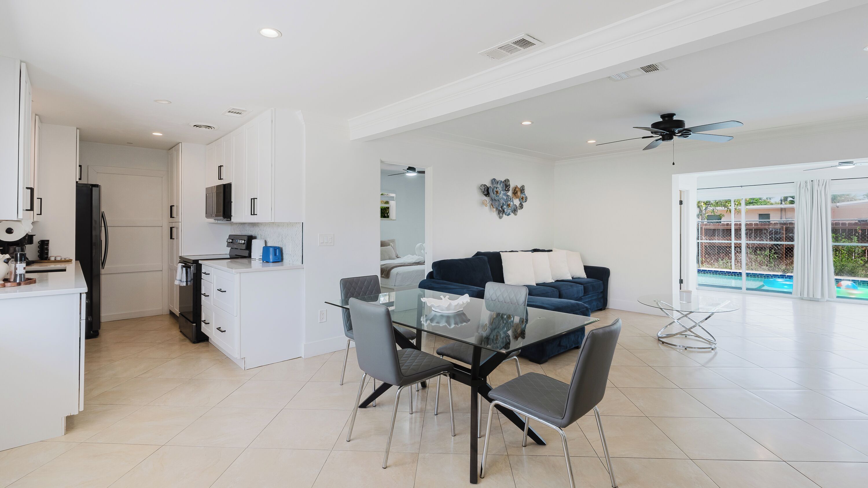 A modern kitchen with white cabinets, a black refrigerator, and a dining area with a glass table and chairs.