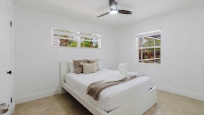 A bedroom with a bed, a ceiling fan, a window, and wall-mounted artwork.