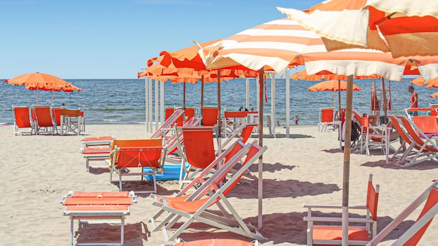 A beach with rows of orange and white striped umbrellas and chairs.
