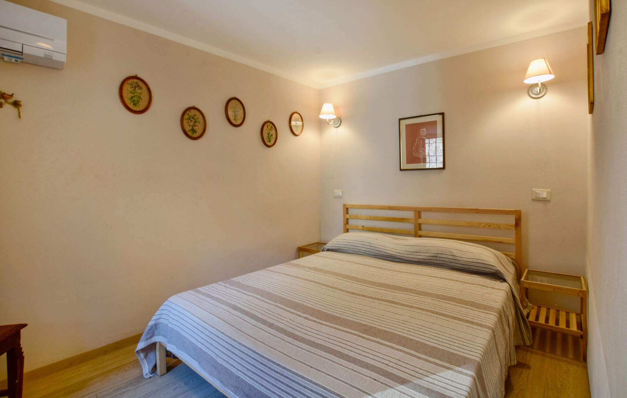 Une chambre à coucher avec un lit en bois, une table de chevet, une lampe fixée au mur et des tableaux encadrés accrochés au mur.