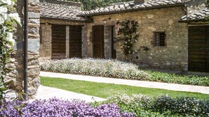 Un bâtiment en pierre avec un toit recouvert de tuiles, un jardin où poussent des fleurs blanches et violettes, et un ciel dégagé.