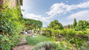 Un exuberante jardín con un camino de ladrillo que conduce a un espacio de descanso con una mesa y sillas.