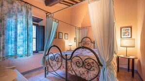 Un lit à baldaquin avec une couvre-lit à motifs floraux, une petite table de chevet avec une lampe et un tableau encadré au mur.
